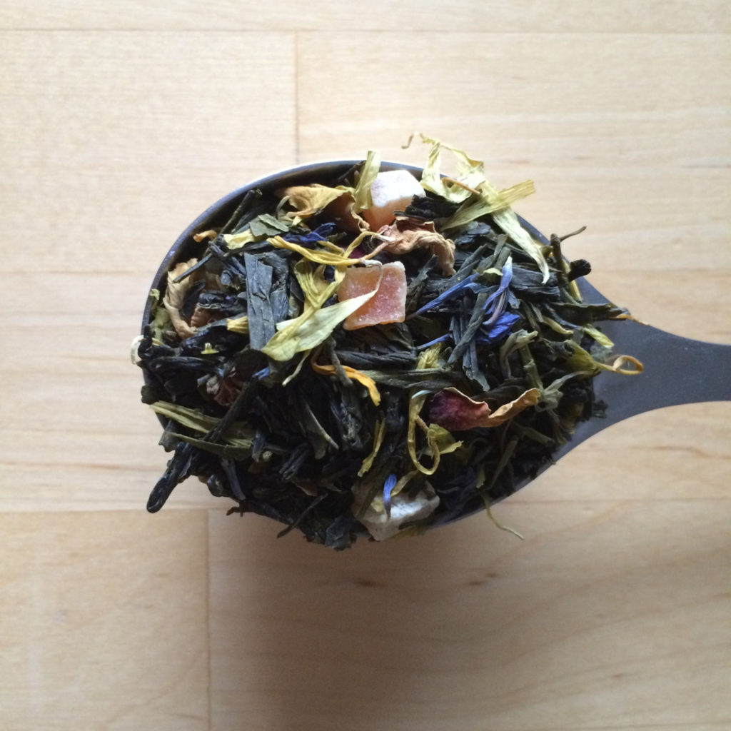 A spoonful of blended green tea with fruit and flower petals